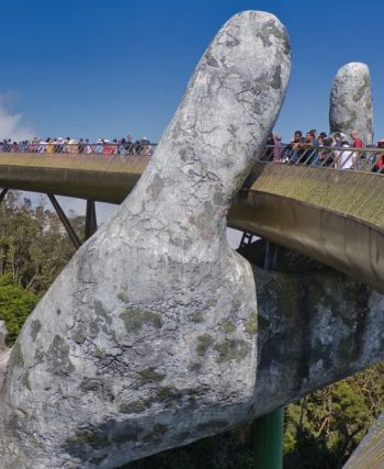 The iconic Golden Bridge with giant hand sculptures at Ba Na Hills, Vietnam, under a clear blue sky.