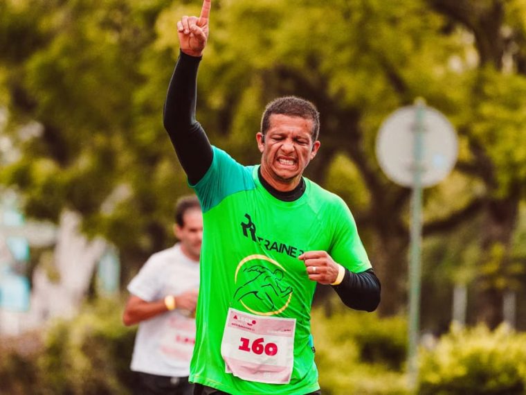 Joyful male runner celebrates a marathon win outdoors, raising arms in triumph.